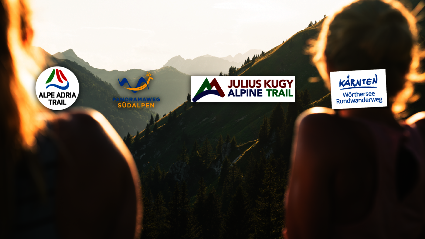<p>Bild zweier Wanderinnen im Sonnuntergang mit Gebirgslandschaft. Darauf die Logos der Weitwanderwege Alpe-Adria-Trail, Panoramaweg Südalpen, Julius-Kugy-Alpine-Trail und Wörthersee Rundwanderweg. </p>